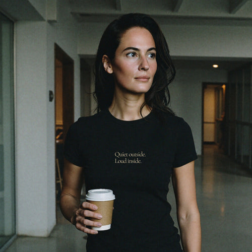 Woman in Question Everything Co. black tee reading Quiet outside. Loud inside. in work corridor.